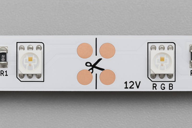 A close-up image of an LED strip showing the clearly marked cut line with a scissor icon, flanked by the essential copper solder pads.