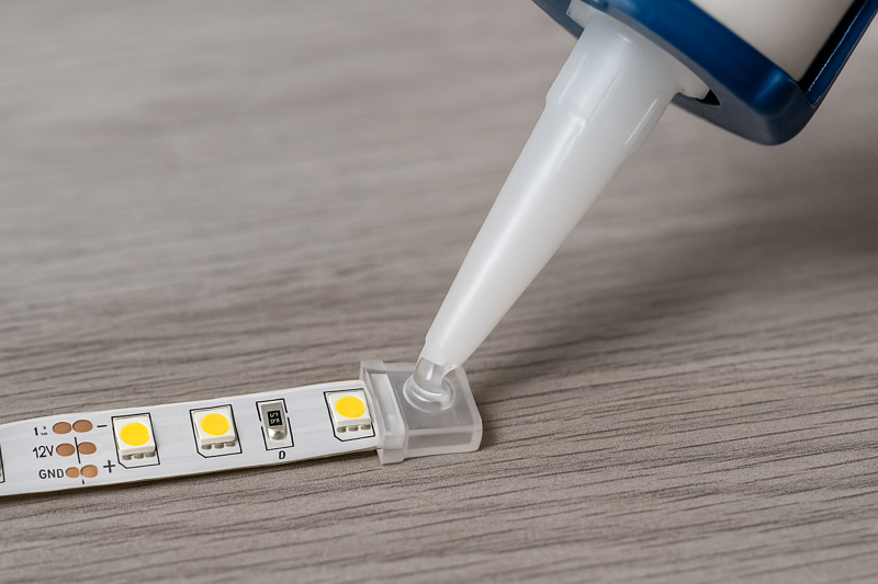 A detailed image of silicone sealant being applied to an LED strip end cap before attachment