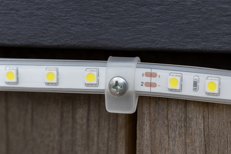 A close-up of a silicone mounting clip holding an outdoor LED strip in place with a screw