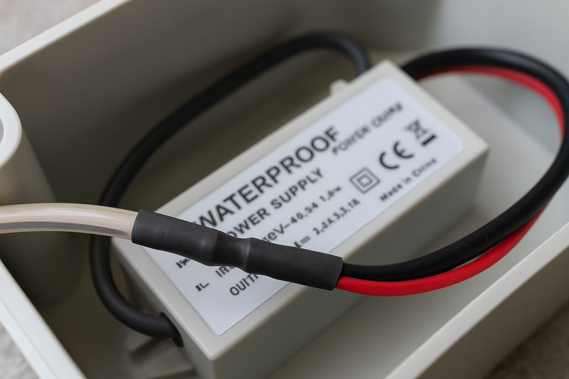 A close-up shot showing a properly sealed connection using adhesive-lined heat shrink tubing, with a waterproof power supply visible in the background inside a junction box.