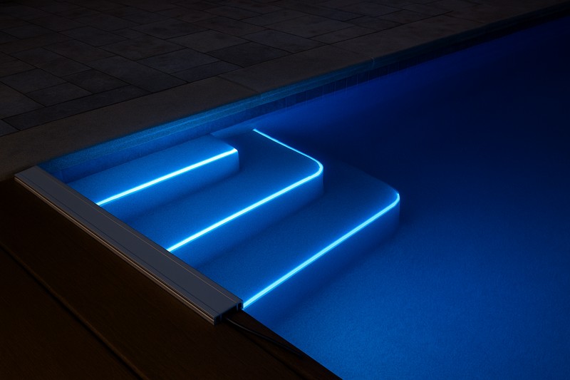 A stunning shot of an IP68 LED strip illuminating the underwater steps of a luxury swimming pool at night, casting a clear, brilliant blue light through the water.