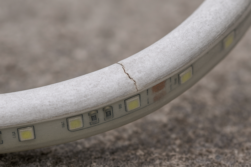 A photo of a PVC-jacketed light that has been installed outdoors. The surface looks chalky and faded, and there's a visible crack near a bend that occurred during a cold winter.