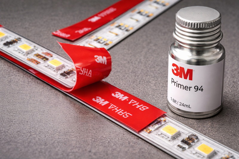 Close up of 3M VHB tape (Red liner) applied to an LED strip, next to a bottle of 3M Primer 94.
