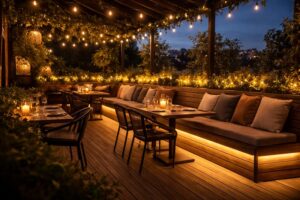 A warm, inviting restaurant patio at twilight. Soft, golden light glows from under the bench seating and along the fence rails, creating an intimate atmosphere