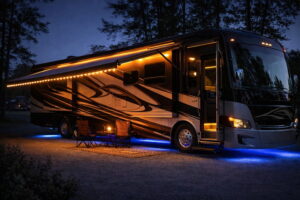 A luxury Class A motorhome parked at a campsite at twilight, featuring warm amber awning lights and soft blue underglow lighting, creating a cozy atmosphere