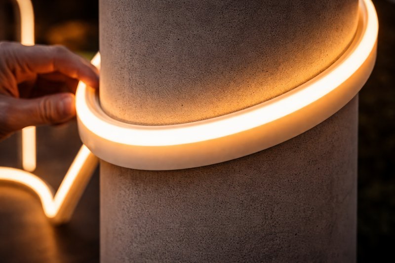 Close up of a flexible Silicone Neon strip being bent around a curved concrete pillar, emitting a smooth, dot-free glow.