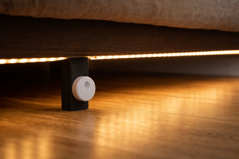 Image showing the underside of a bed frame with an LED strip mounted, illustrating the motion sensor placement near the floor.