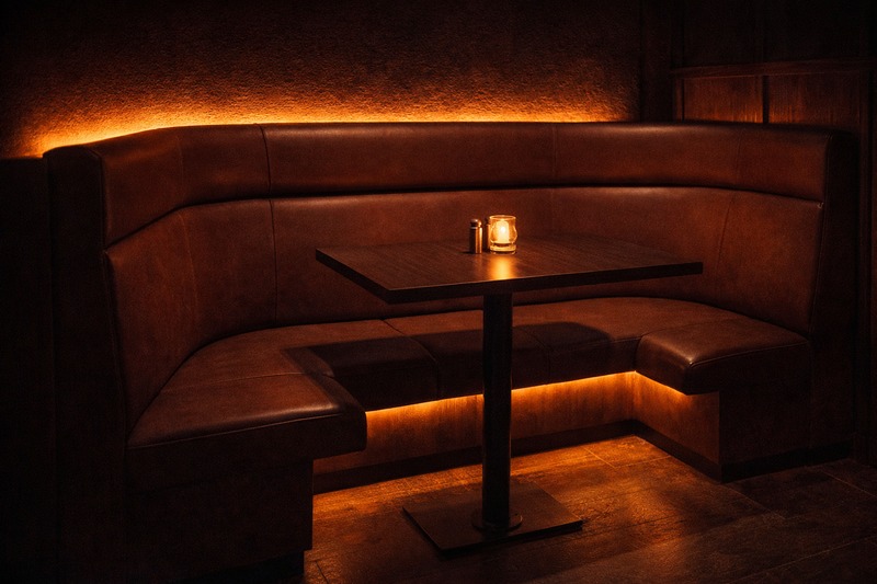 Photo of a cozy booth seating area with soft, warm light glowing from underneath the bench and behind the headrest, creating a private feel.
