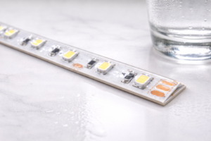 Close up photo: A basic IP65 strip with a domed silicone top layer on a white counter, next to a glass of water.