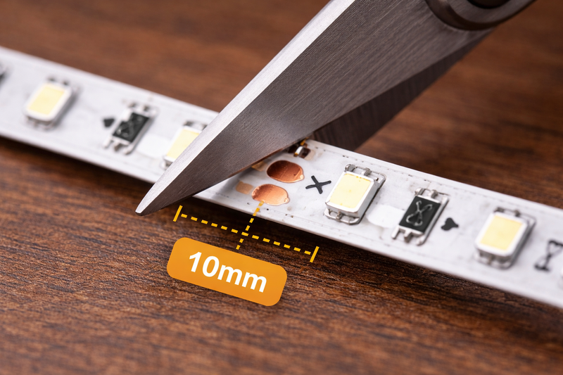 Macro photo of a scissor cutting an LED strip at a tiny copper pad labeled 