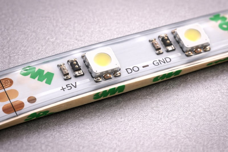 Macro Photo: Close up of an IP65 strip. You can see the dome of clear silicone over the yellow chips, but the back adhesive is visible.